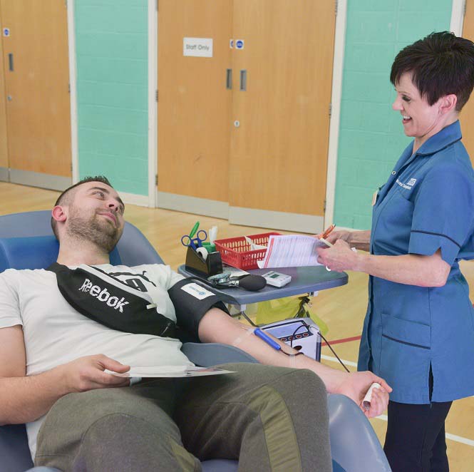 A blood donor sits in a reclined donor chair