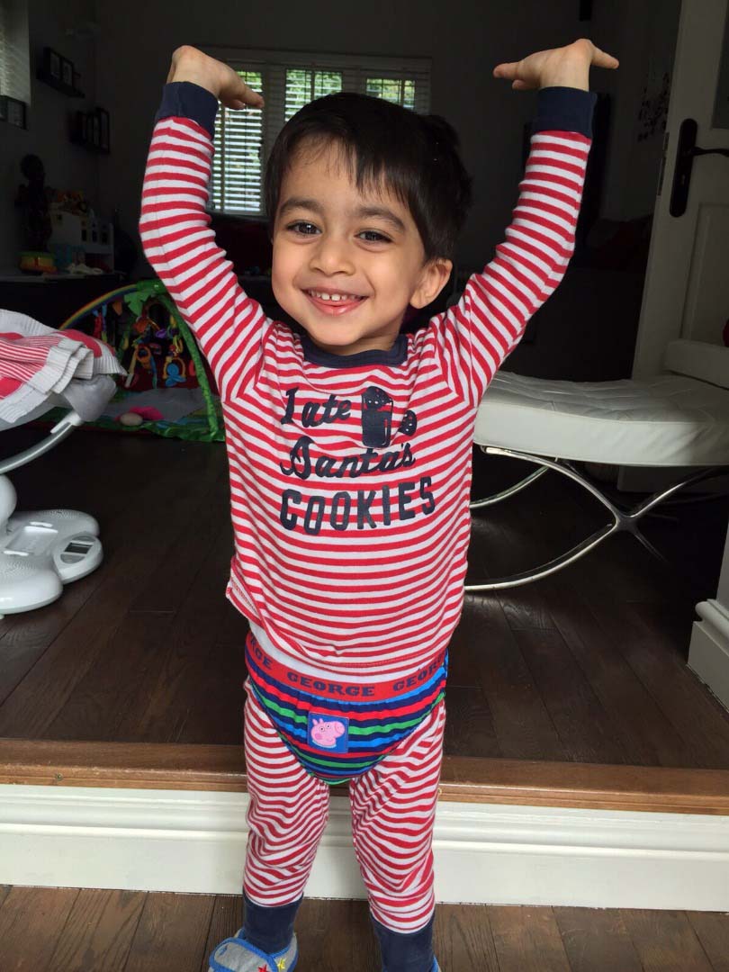 Aari wearing 'I ate Santa's cookies' pyjamas, with his hands in the air and smiling