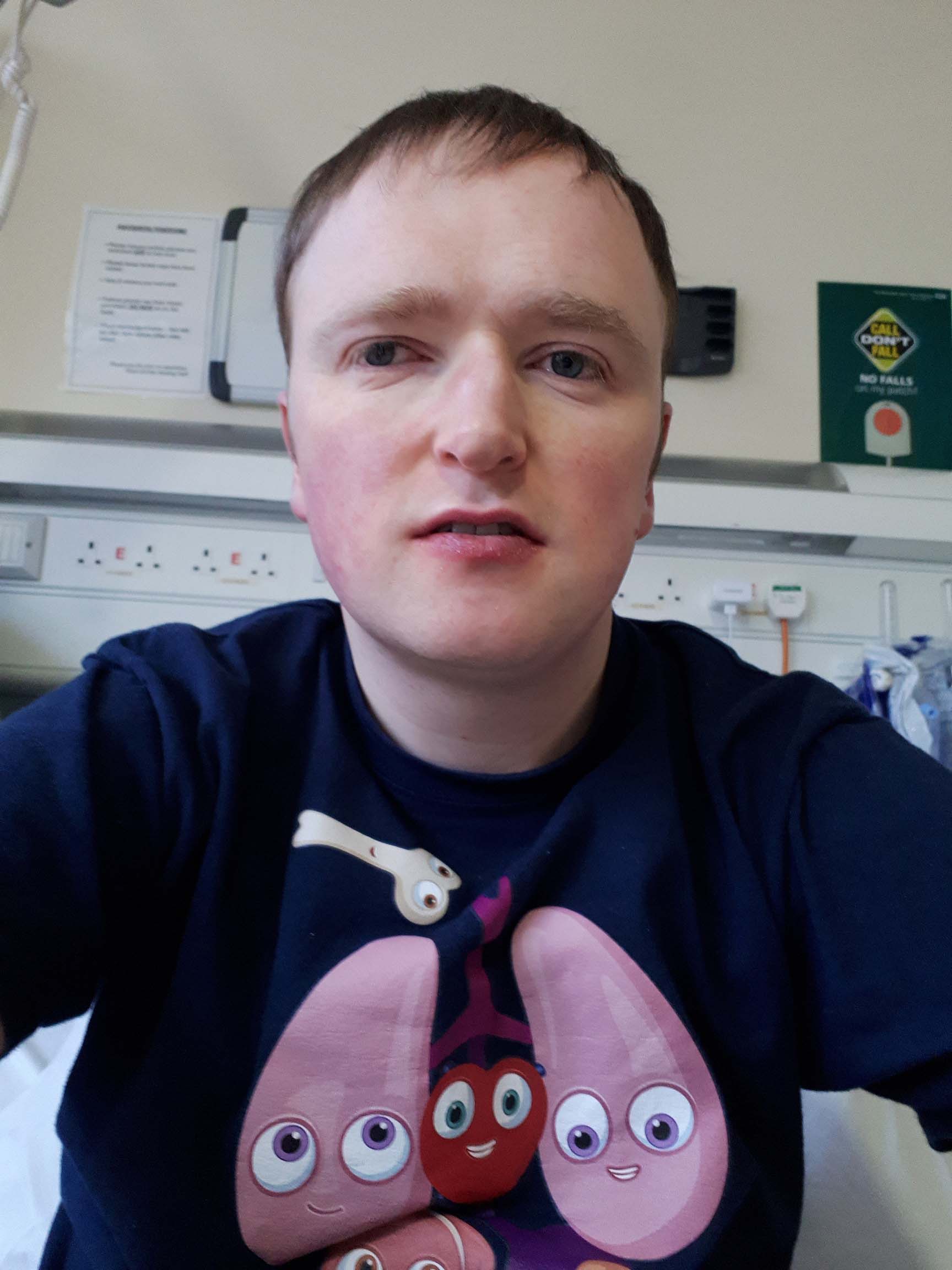 Patrick sits on a hospital bed wearing an organs t-shirt