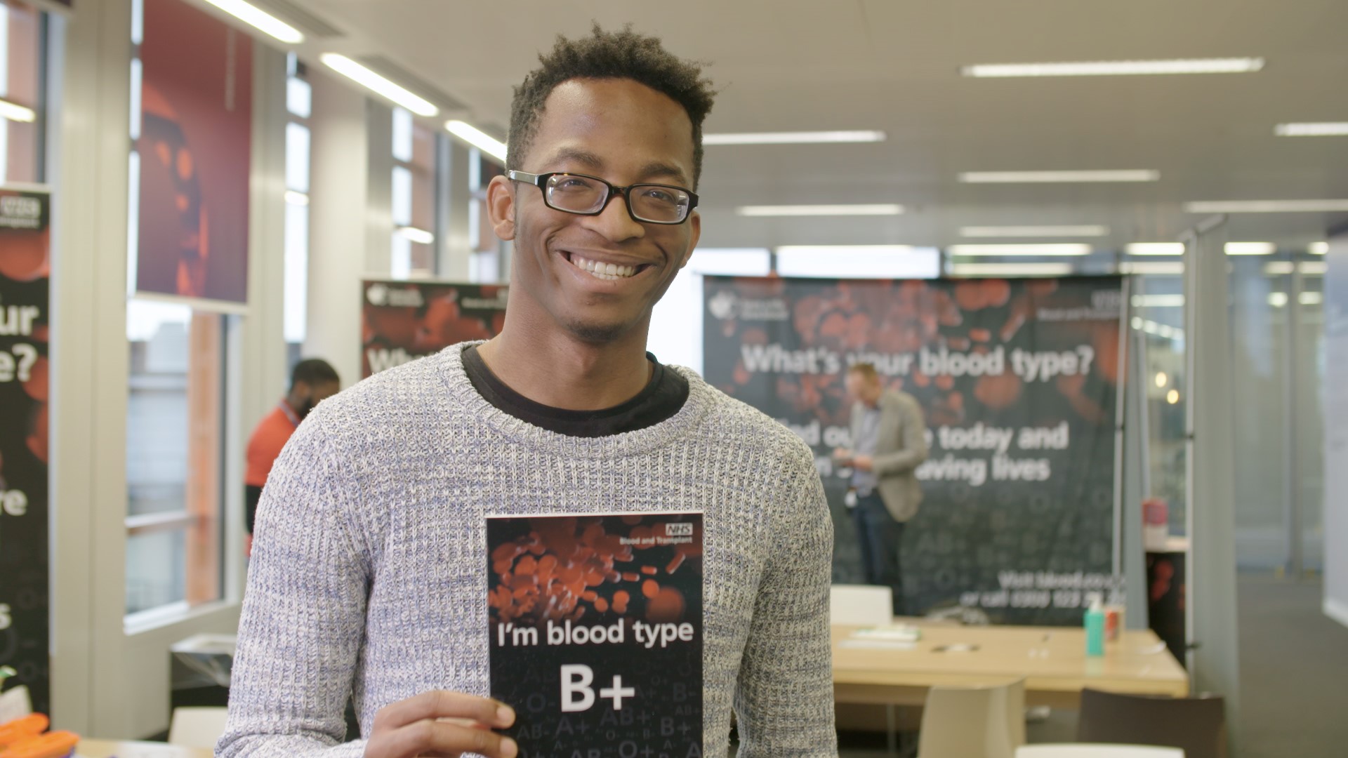 A young man holds a card that says, "I'm blood type B+"