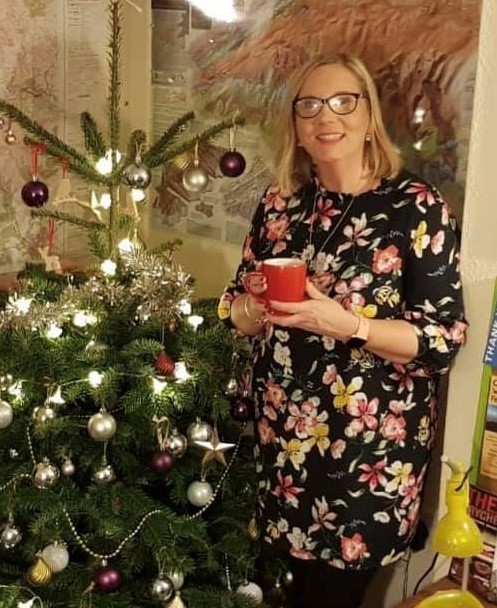 Donna stands next to a Christmas tree with a hot drink