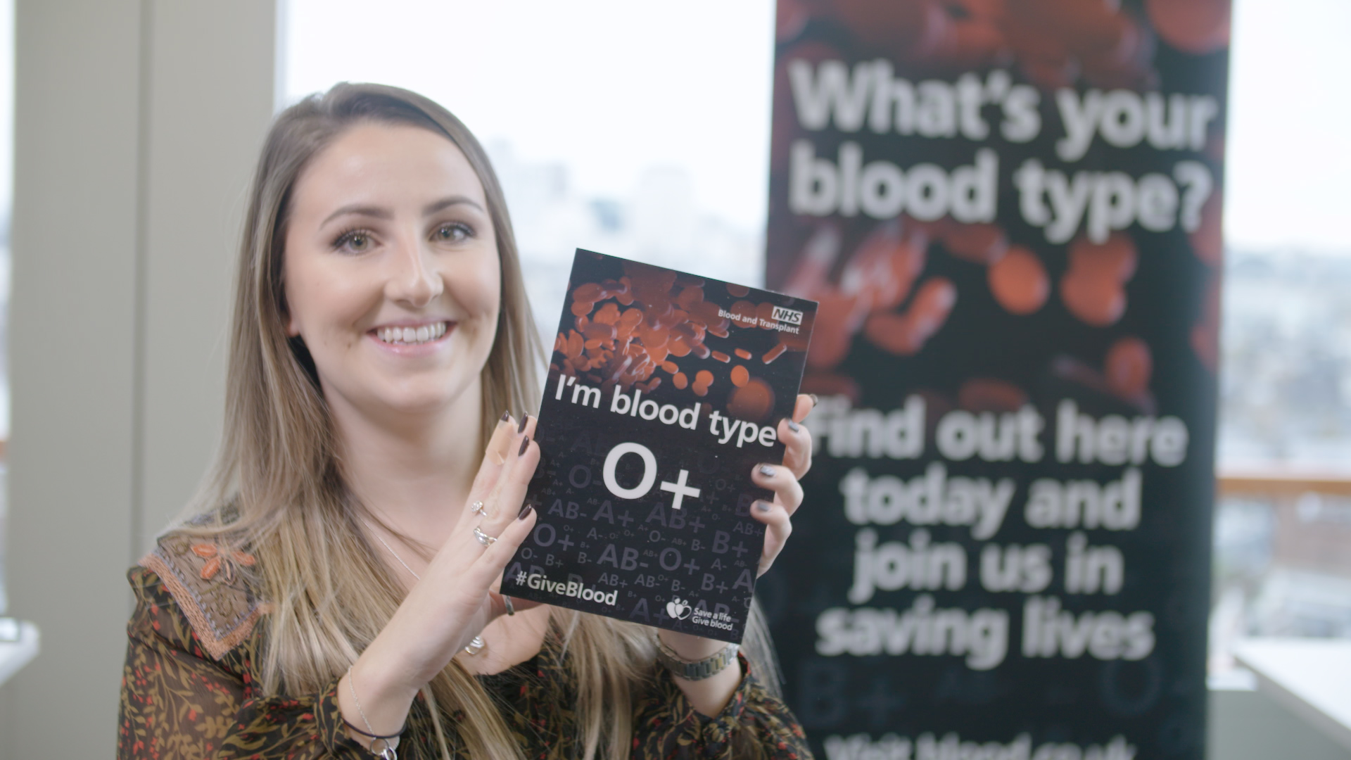 A young woman poses with a card that says, "I'm blood type O+"