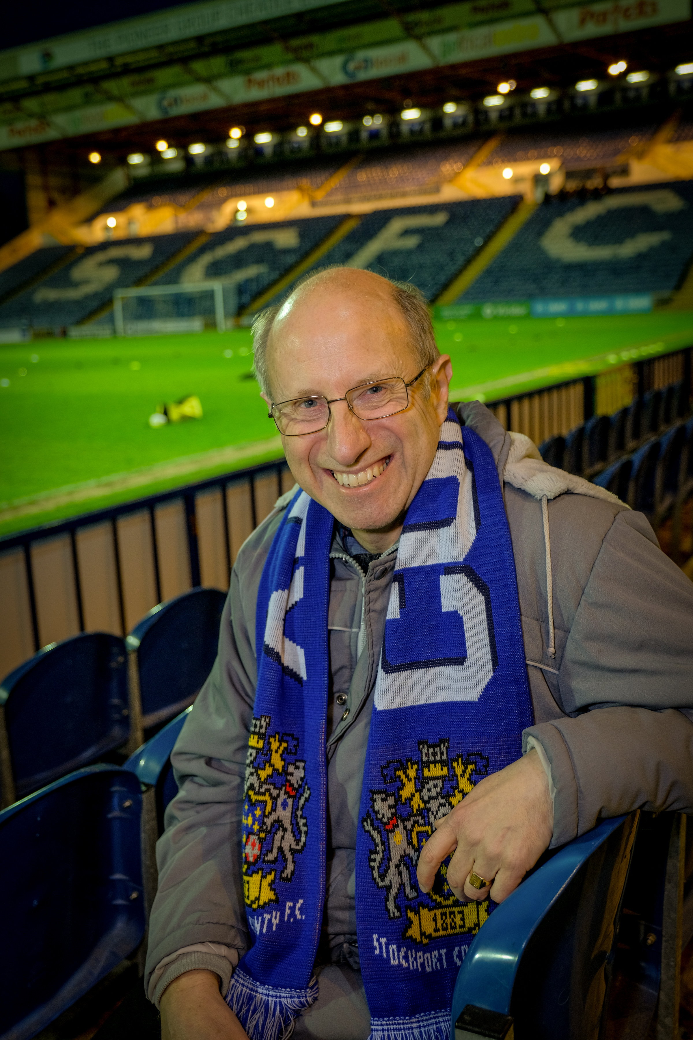 Steve, wearing a football scarf, sits in an empty football stadium