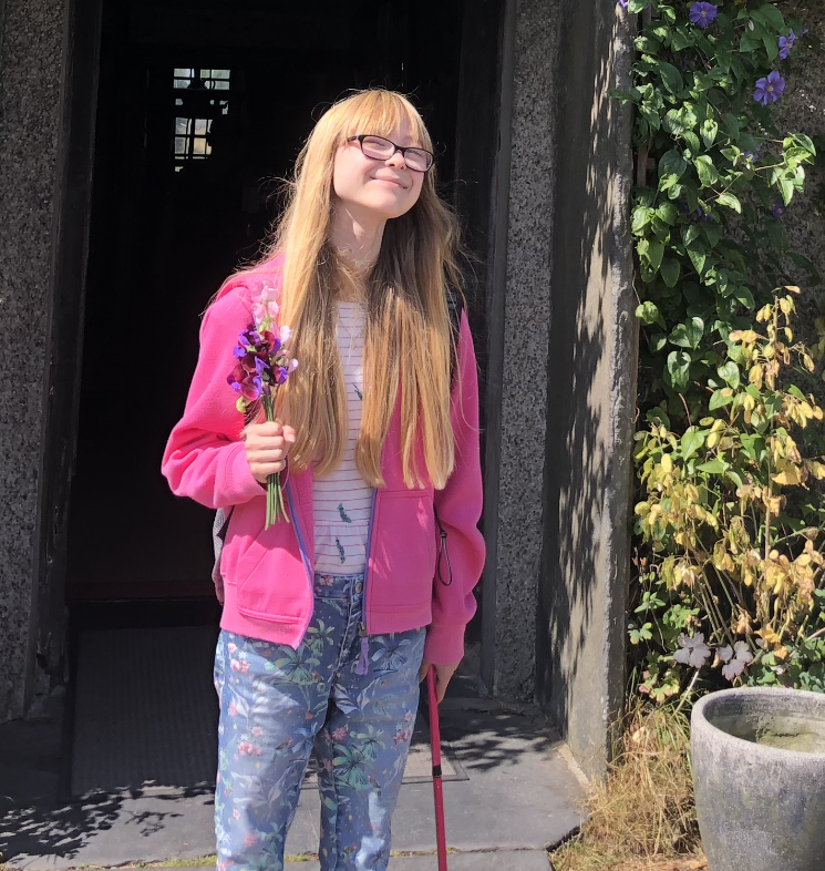 Angharad staat in een zonnige tuin en houdt een klein bosje bloemen vast