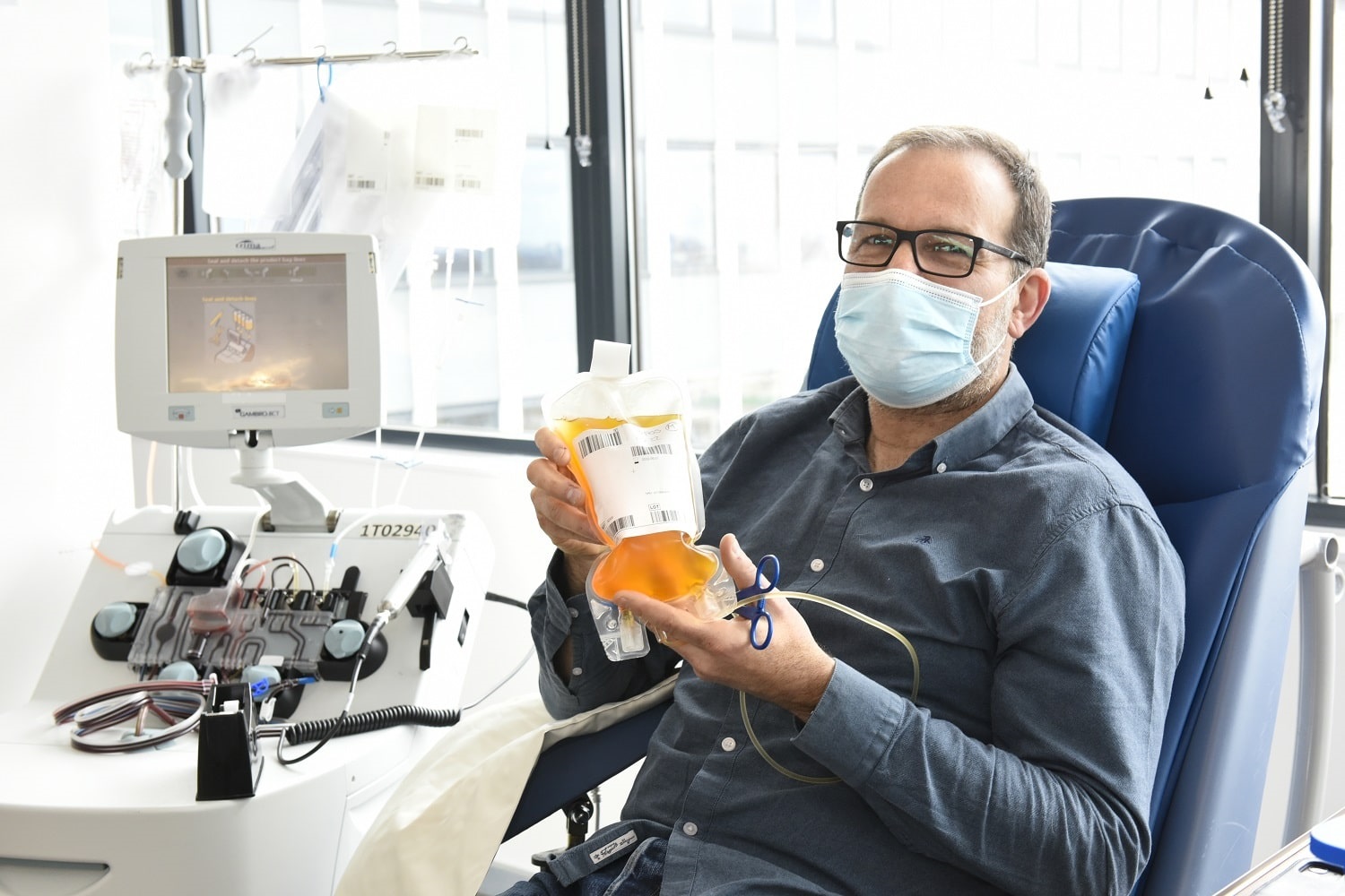A man sitting in a donor chair holds a bag of his plasma