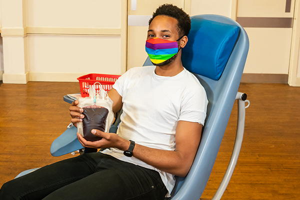 LGBT donor holding recently donated bag of blood in chair