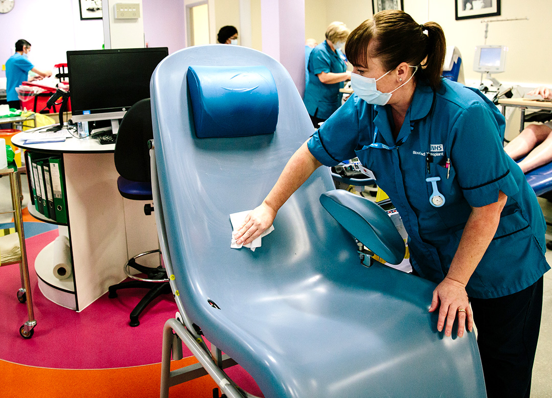 A donor carer in a face mask cleans a donation chair