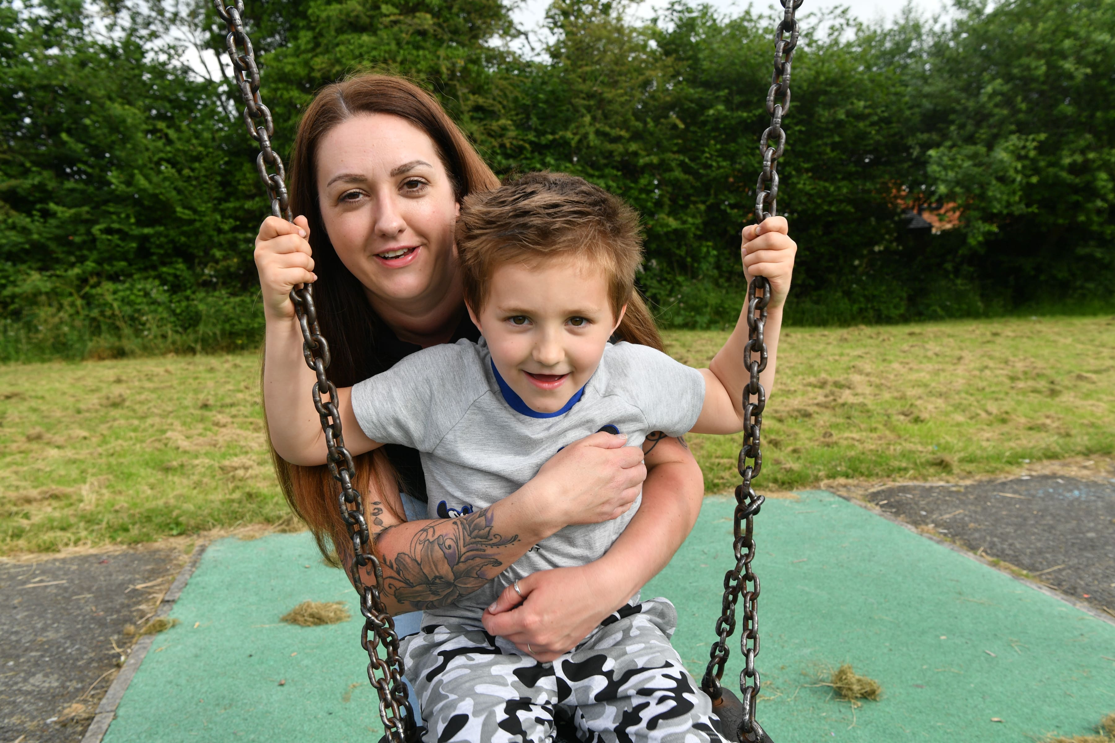Harley sits on a swing while his mum hugs him