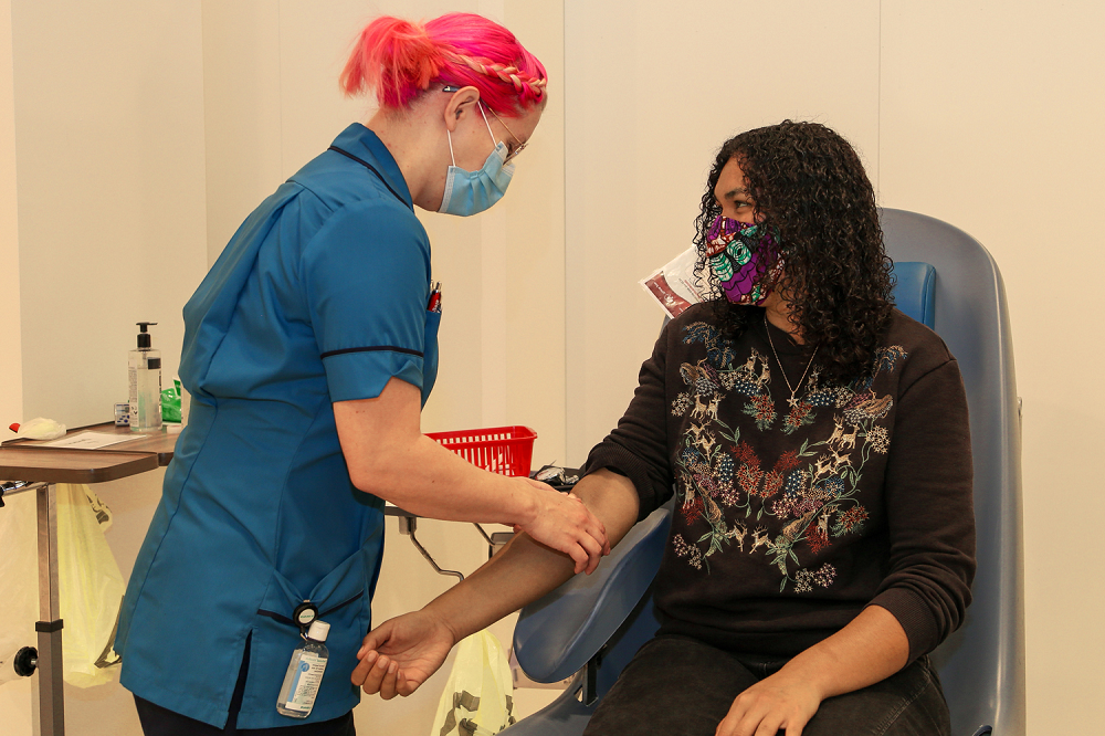 Female donor carer taking blood donation from female donor