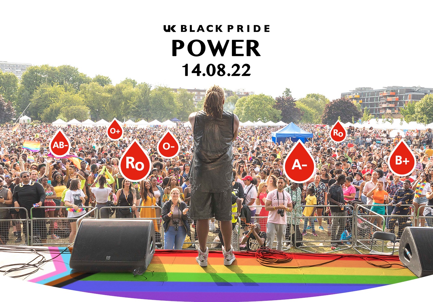 Man performing on stage at Pride festival. Some audience members have their blood group labelled
