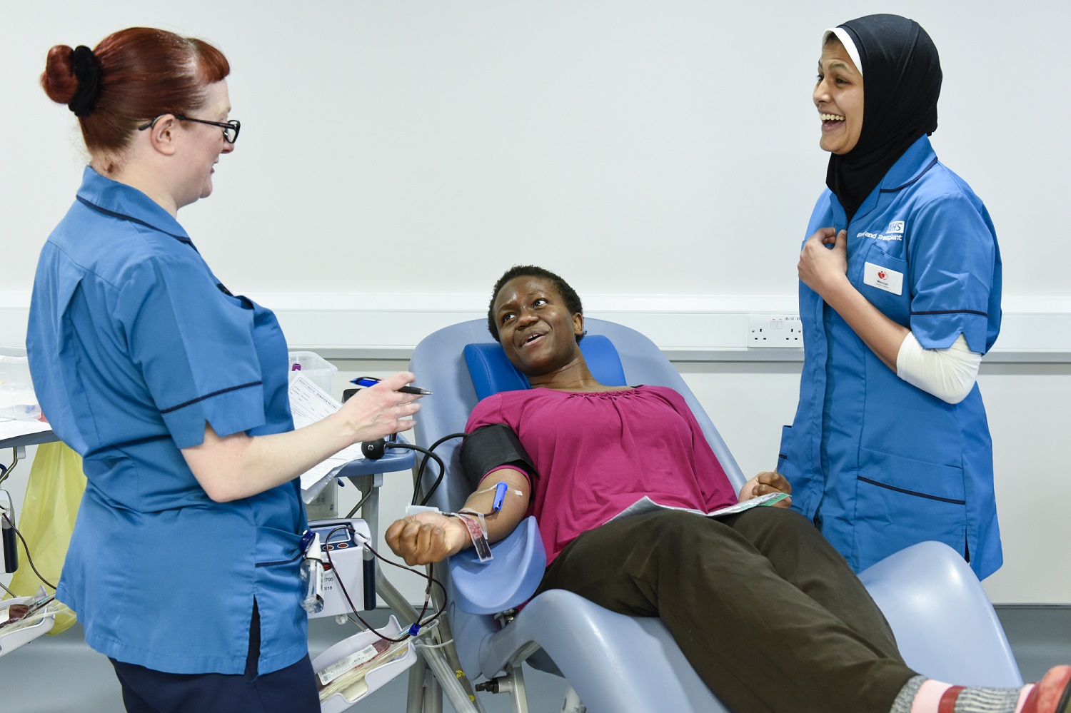 A blood donor donating blood, looked after by two Blood Donation Healthcare Assistants