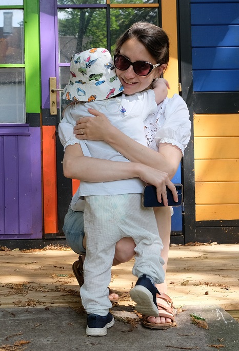 Katie kneeling down to hug her son Ralph, outside on a sunny day