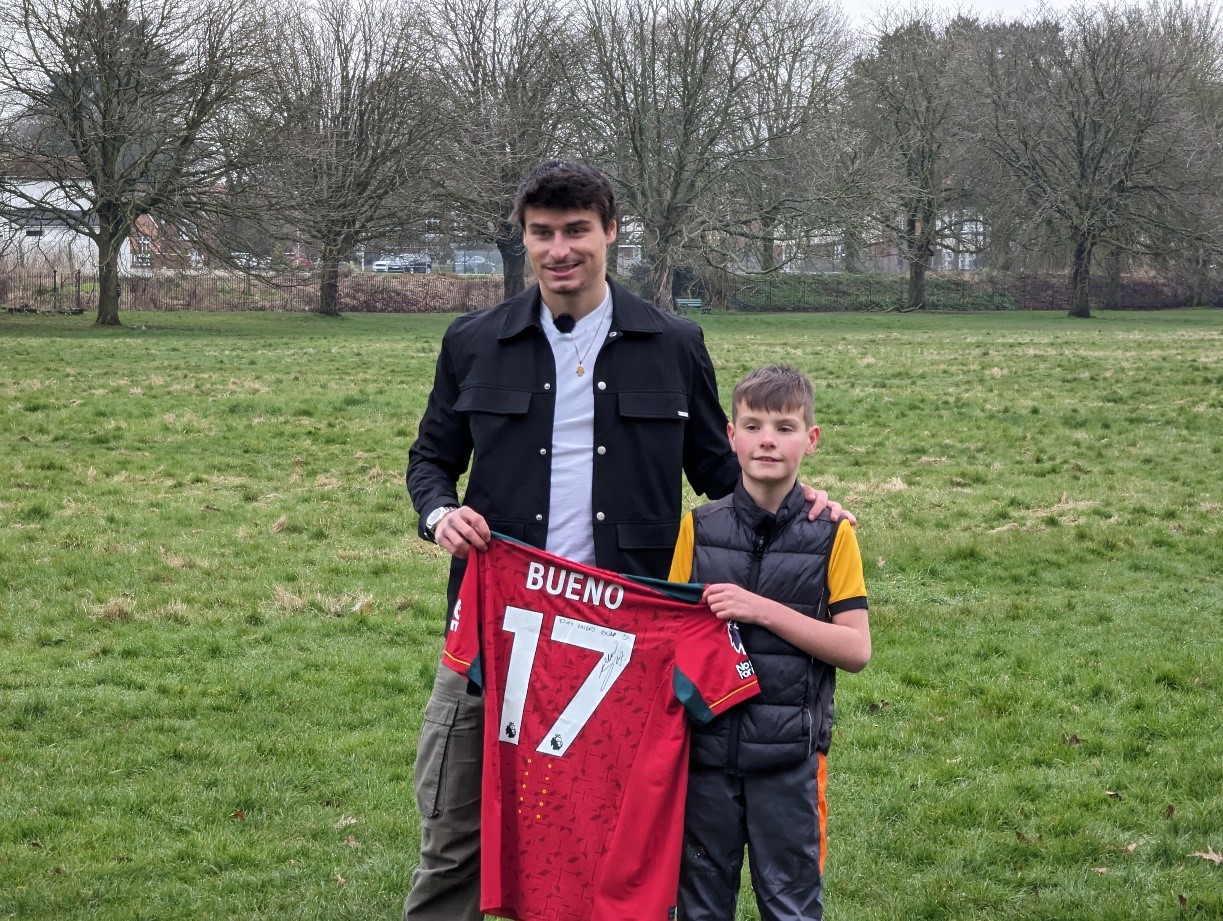 Wolves player Hugo Bueno standing with Oscar and holding a signed football shirt