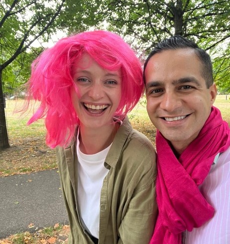 A picture of two people wearing pink to celebrate. Sasha, on the left, wearing a pink wig with Ali, on the right, wearing a pink scarf