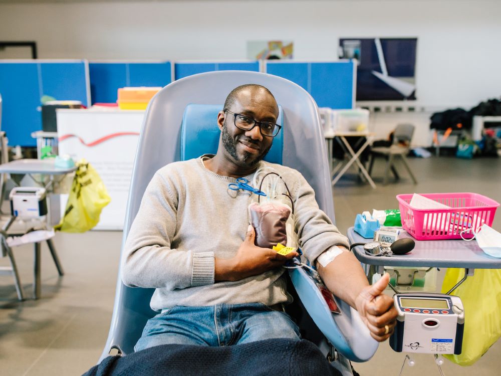 Donor giving blood and holding their blood donation bag