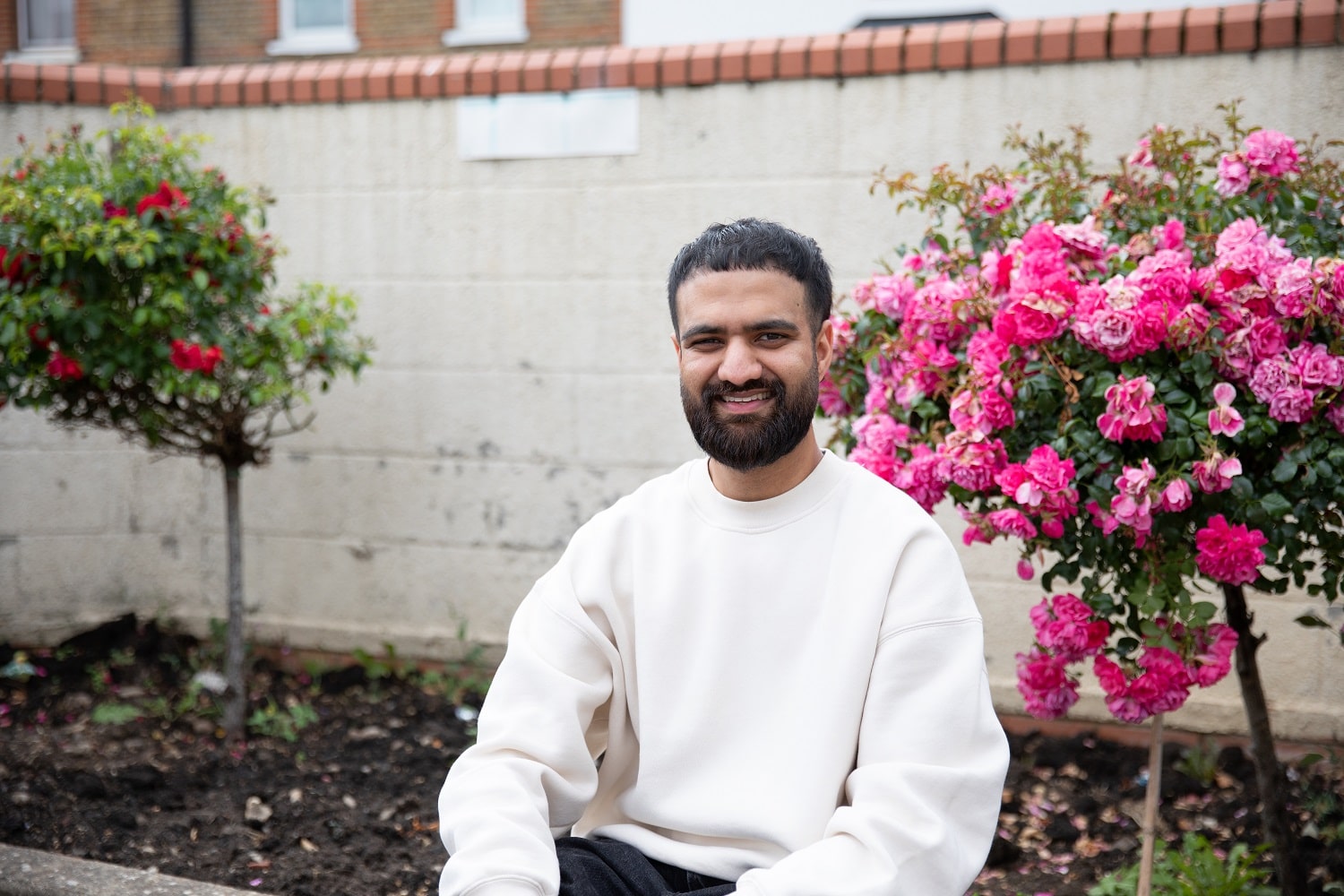 Abrar sat on the edge of a flower bed smiling at the camera