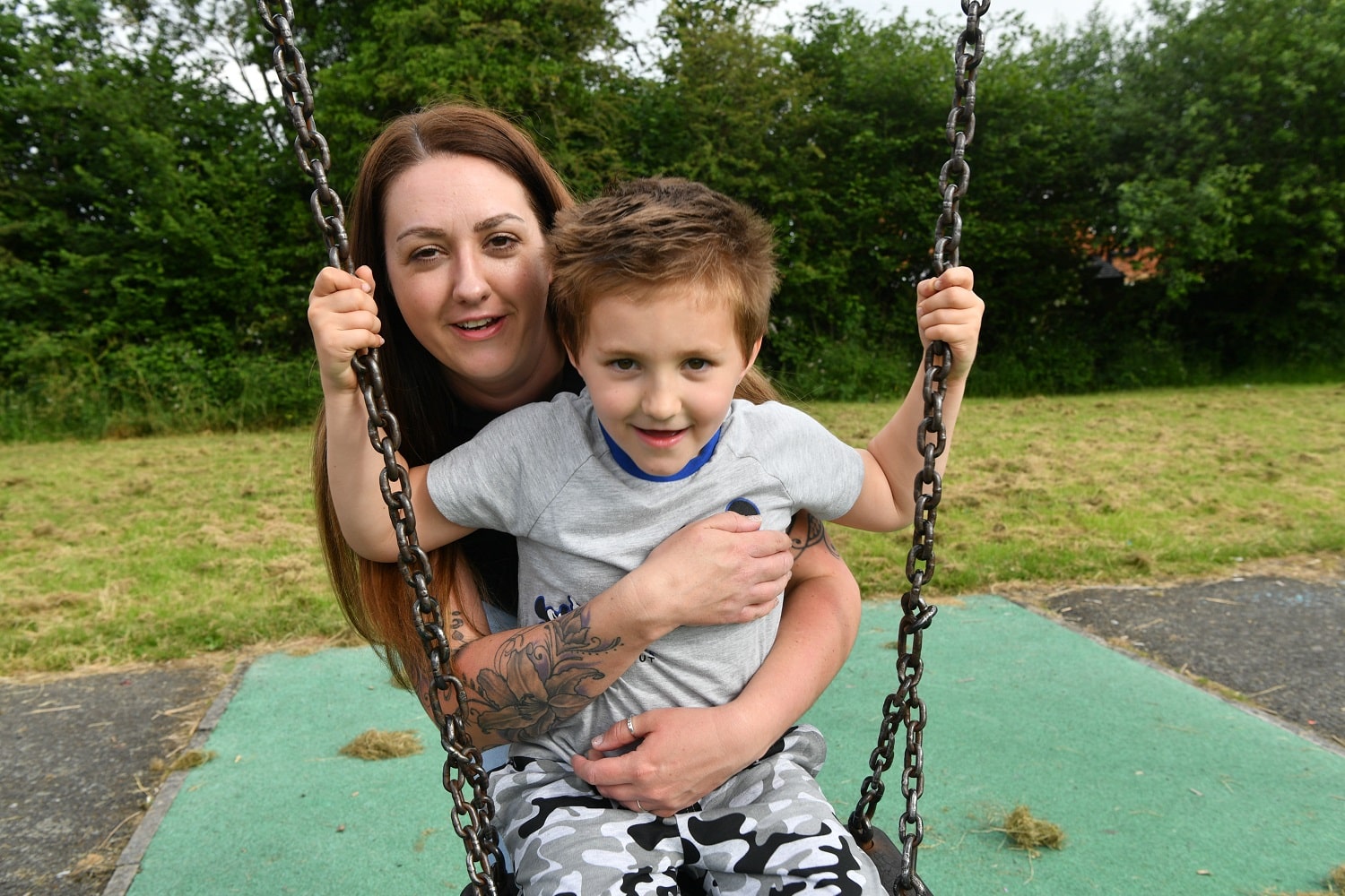 Harley sits on a playground swing whilst his Mum, Leanne, hugs him from behind