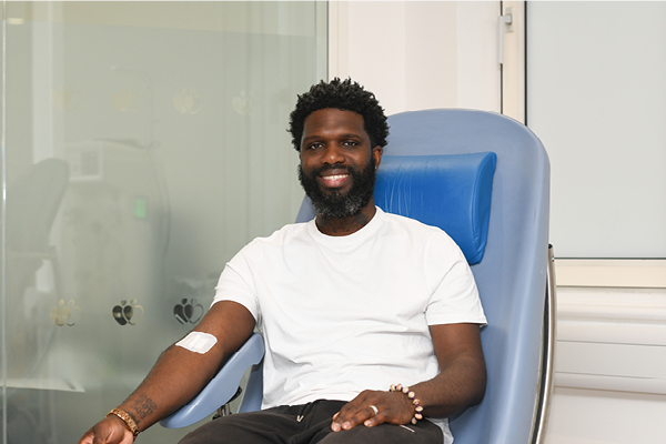 A man of Black heritage smiles in donation chair after just donated, a plaster on his arm.