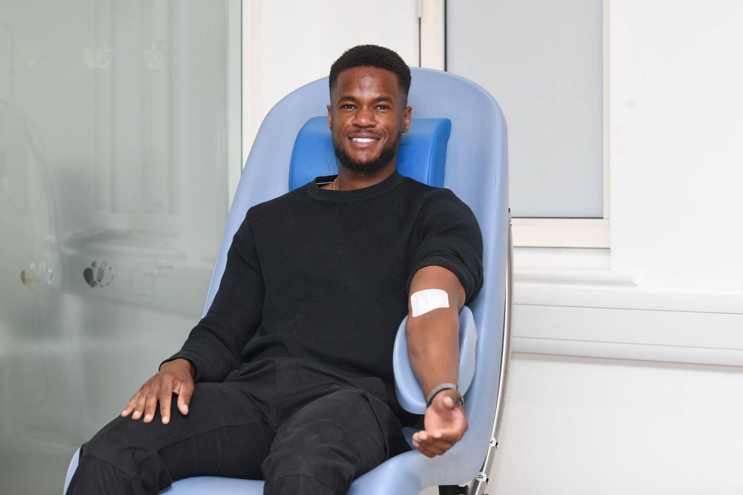 A Black heritage man in a clinic chair with a bandage on his arm after donating blood.