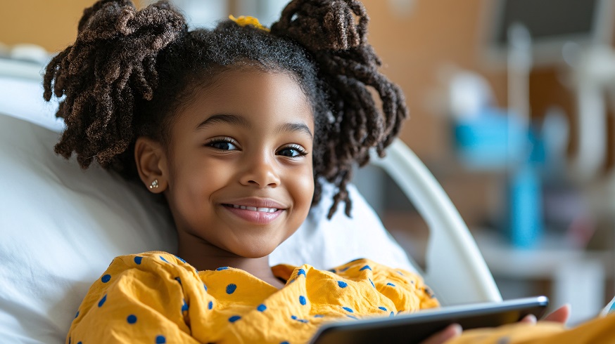 A youong girl in a hospital bed, holding a tablet and smiling