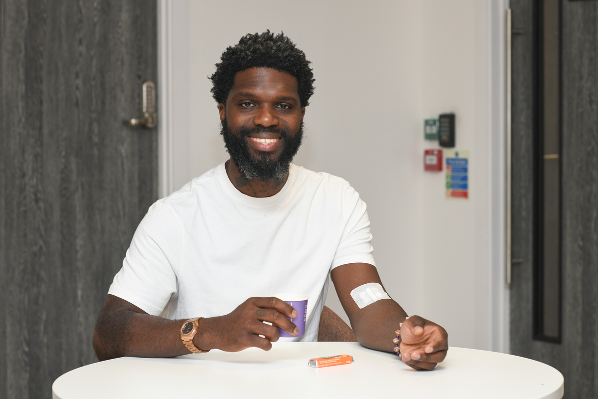 A donor sits at at a table after donating with a drink and club biscuit, a plaster on his arm