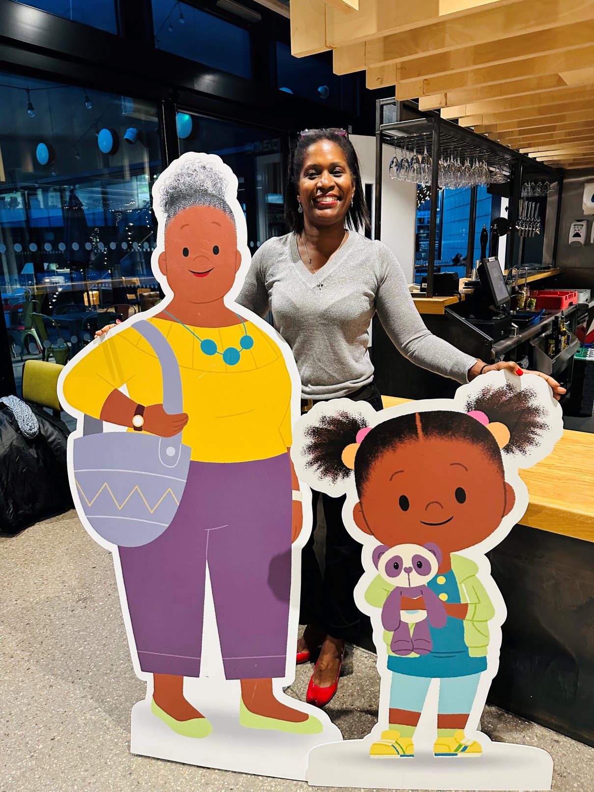 Laura Henry-Allain MBE standing behind 2 cartoon character cutouts.
