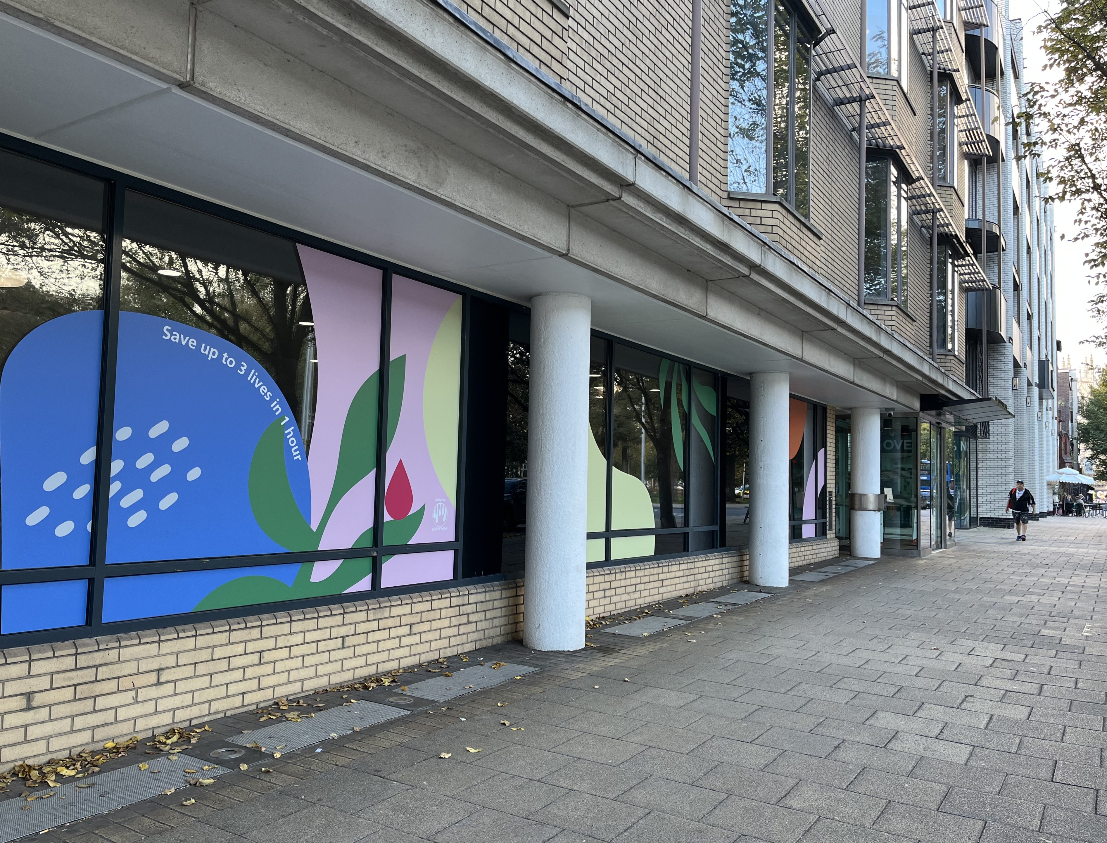 Exterior photo of the Brighton donor centre, showing colourful graphics in the window with the phrase "Save up to 3 lives in 1 hour"