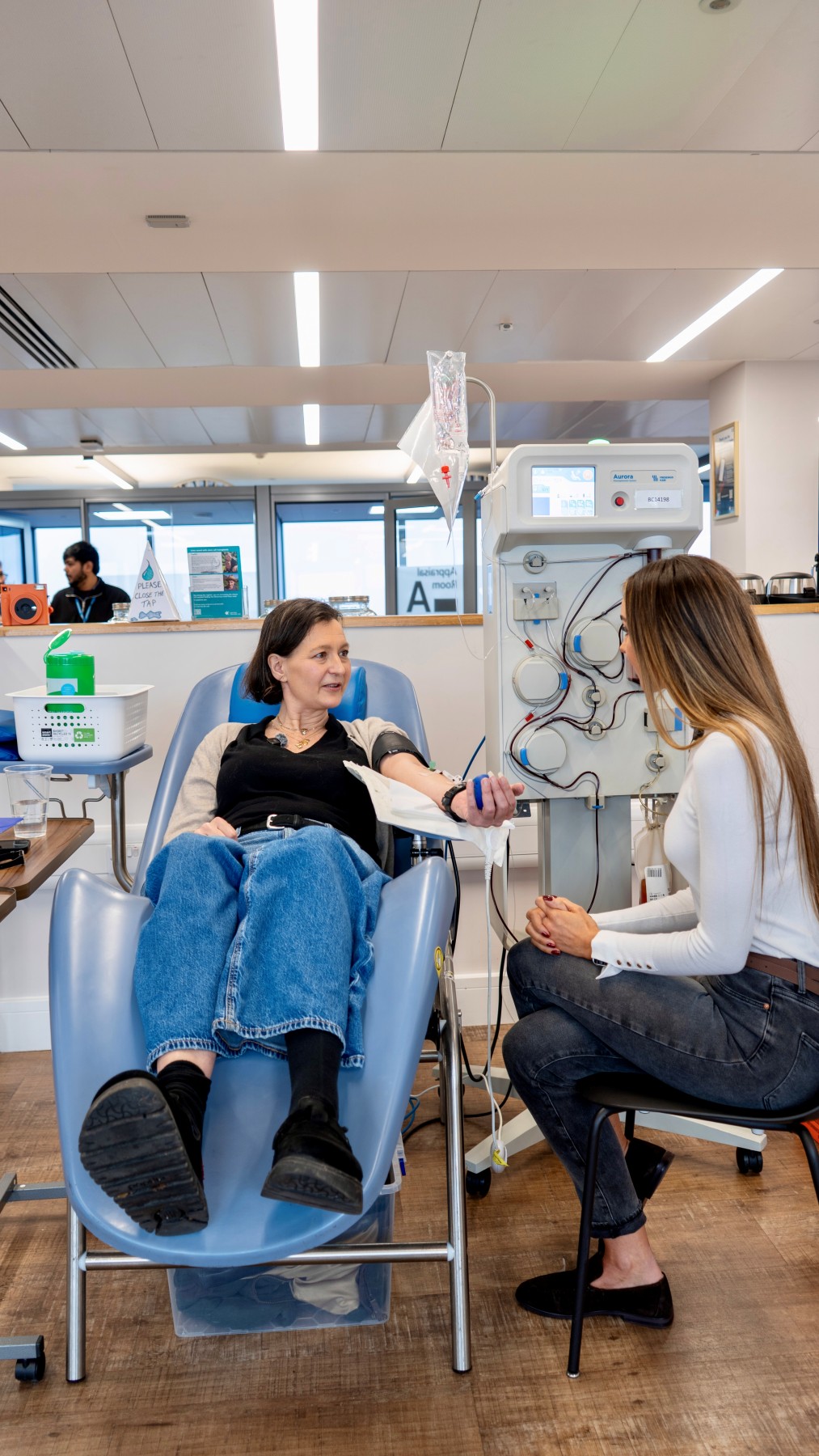Rebecca sitting in a donation chair, donating plasma, while talking to Dr Emily