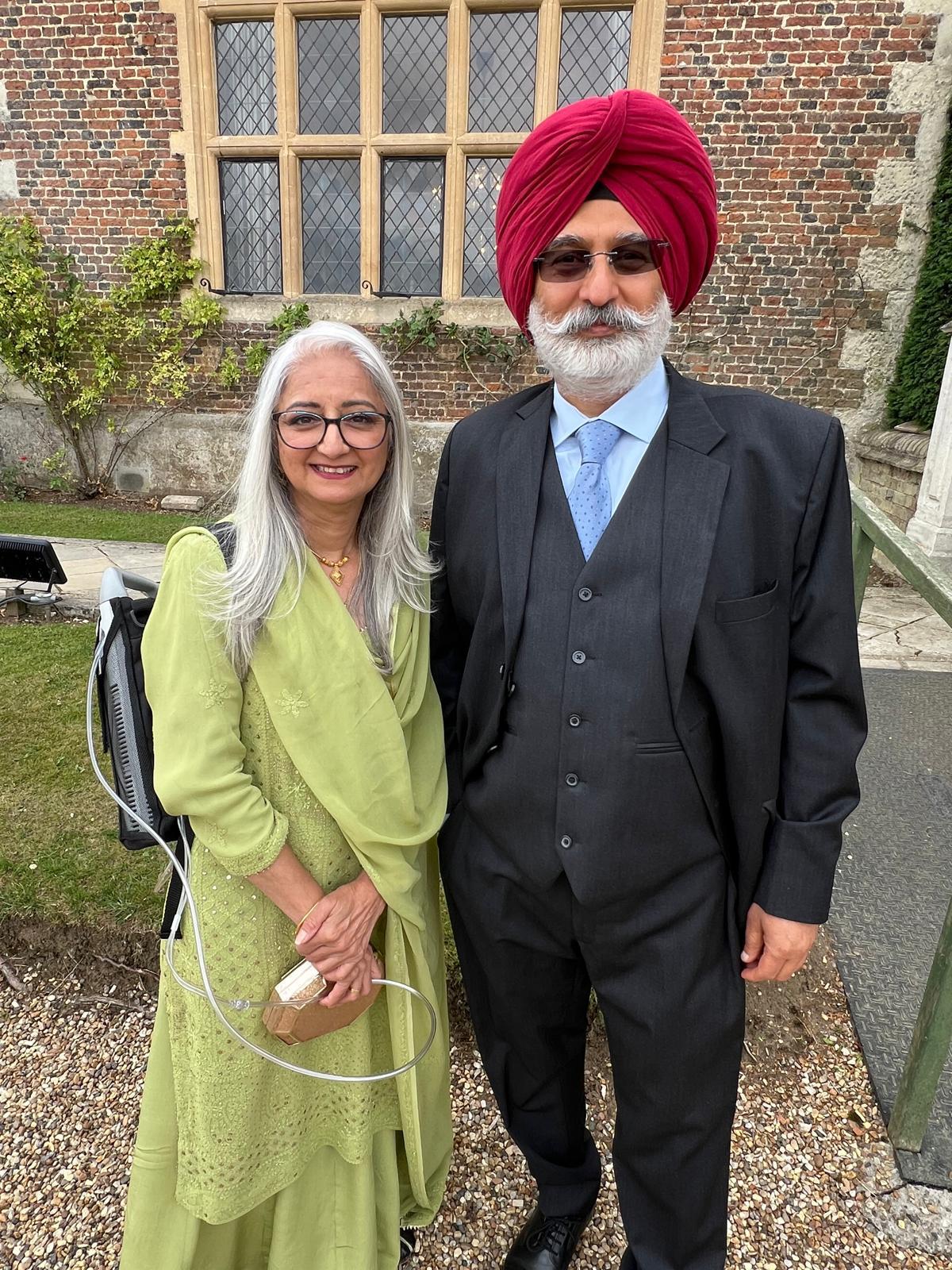 Jaswinder standing on the left side of the image, carrying an oxygen tank on her back standing next to her husband who is standing on the right side of the image