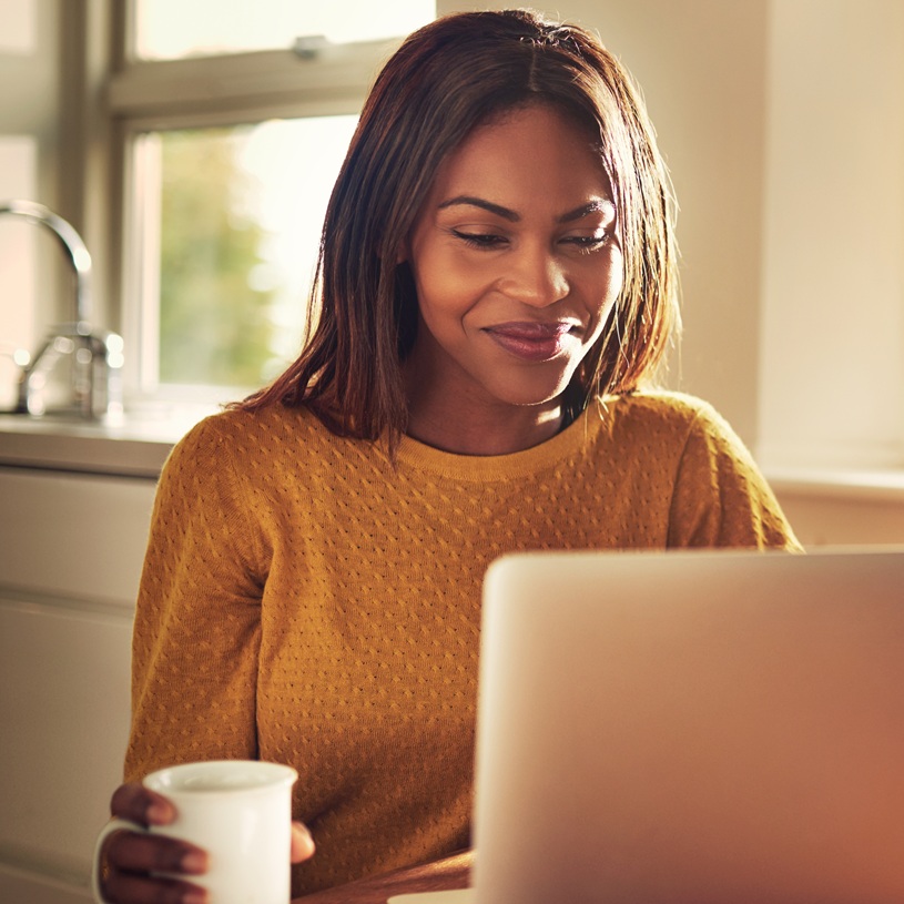 A woman using a laptop while holding a hot drink